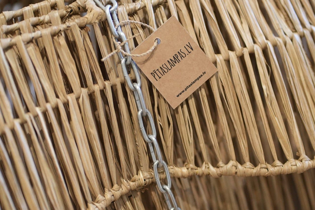 Close-up of a woven lampshade with a PītasLampas.lv tag: natural material and chain fitting